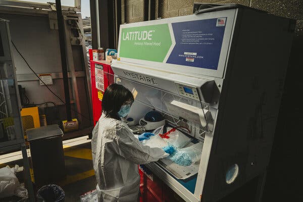 A Customs and Border Protection employee in a white lab coat going through a bag of blue pills.