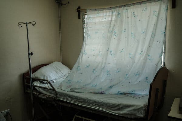 Una habitación con una cama al pie de una ventana desde la que cuelga una cortina larga.