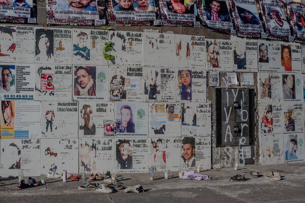 Una pared, cubierta de grandes carteles con nombres y fotos de personas.