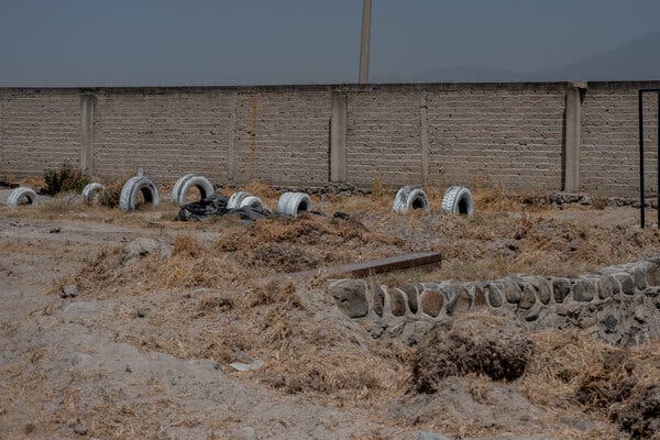 Frente a un muro de bloques de hormigón, hay neumáticos esparcidos por un campo de maleza seca y tierra.