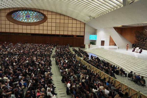 Vista desde arriba de un gran público sentado y del papa en un escenario en un auditorio abovedado.