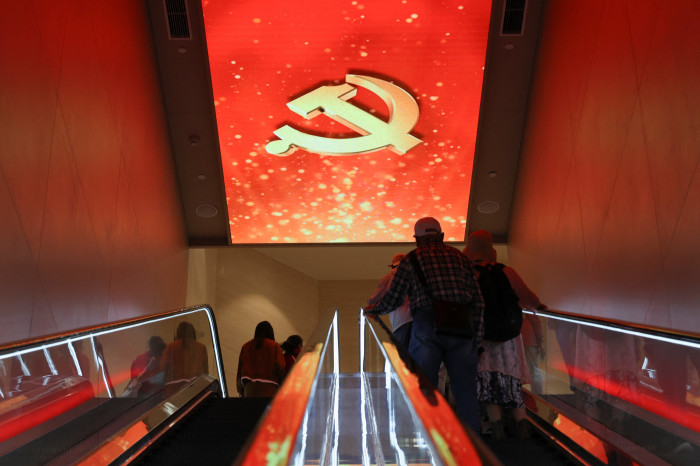 Personas subiendo por una escalera mecánica en el Salón Conmemorativo del Primer Congreso Nacional del Partido Comunista Chino en Shanghai; en el techo se exhibe una gran hoz y un martillo de color rojo.