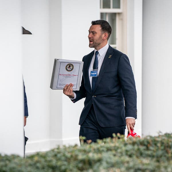 Jack Posobiec en la Casa Blanca mientras sostiene una gorra roja de “Make America Great Again” y una carpeta con la etiqueta “The Epstein Files: fase 1”.