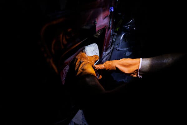 Un par de manos con guantes anaranjados ocultan un paquete en un hueco de la puerta de un vehículo
