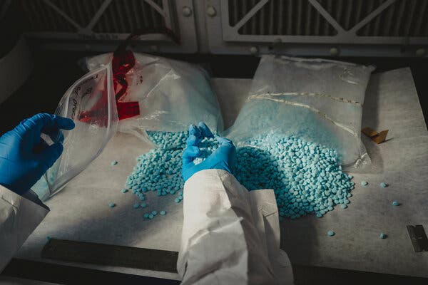 Unas manos con guantes azules sostenían unas pastillas azules que salían de grandes bolsas de plástico.