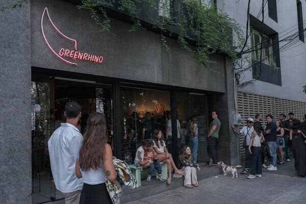Un grupo de personas, incluido un perro pequeño, se encuentra frente a un edificio con un letrero de neón rosa que dice “GREEN RHINO”.