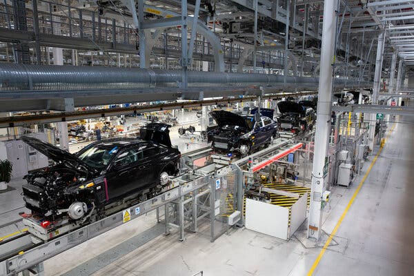 Varios autos negros recorren la línea de una fábrica con el capó abierto.