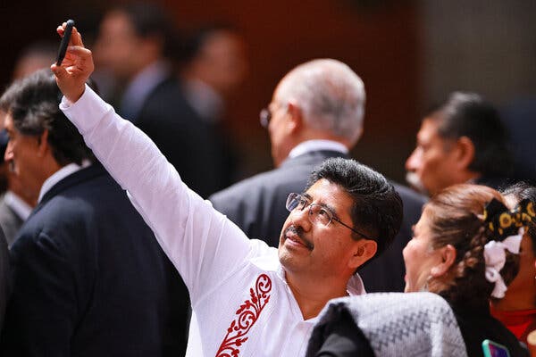 Un hombre con gafas y camisa blanca se hace un selfie con otros.