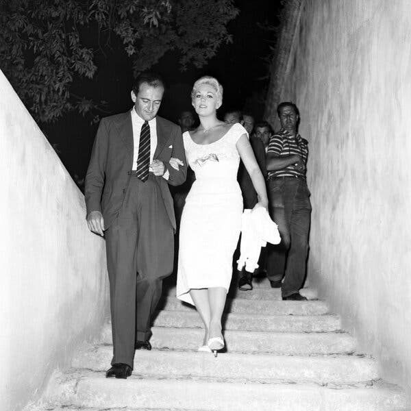 Kim Novak y Mario Bandini bajan unas escaleras con gente detrás.