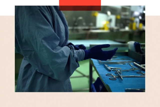 Un cirujano se pone un par de guantes mientras está de pie frente a una mesa sobre la que se han colocado instrumentos quirúrgicos.