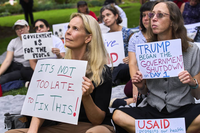 Los manifestantes sostienen carteles sobre el cierre del gobierno, uno que dice “¡No es demasiado tarde para solucionar esto!” y el otro “Trump comenzó el cierre del gobierno el primer día&rdquo.