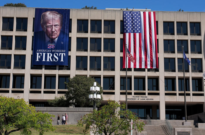Una gran pancarta con una imagen de Donald Trump que dice "Los trabajadores estadounidenses primero" cuelga en el edificio del Departamento de Trabajo, junto a una gran bandera estadounidense.