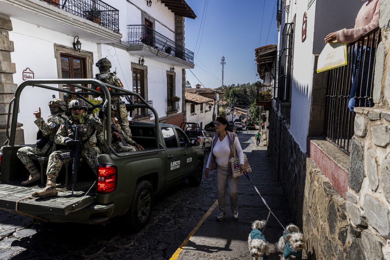 Soldados del ejército mexicano patrullan el centro de Tapalpa en una camioneta militar mientras una mujer pasea a dos perros pequeños junto a ellos.