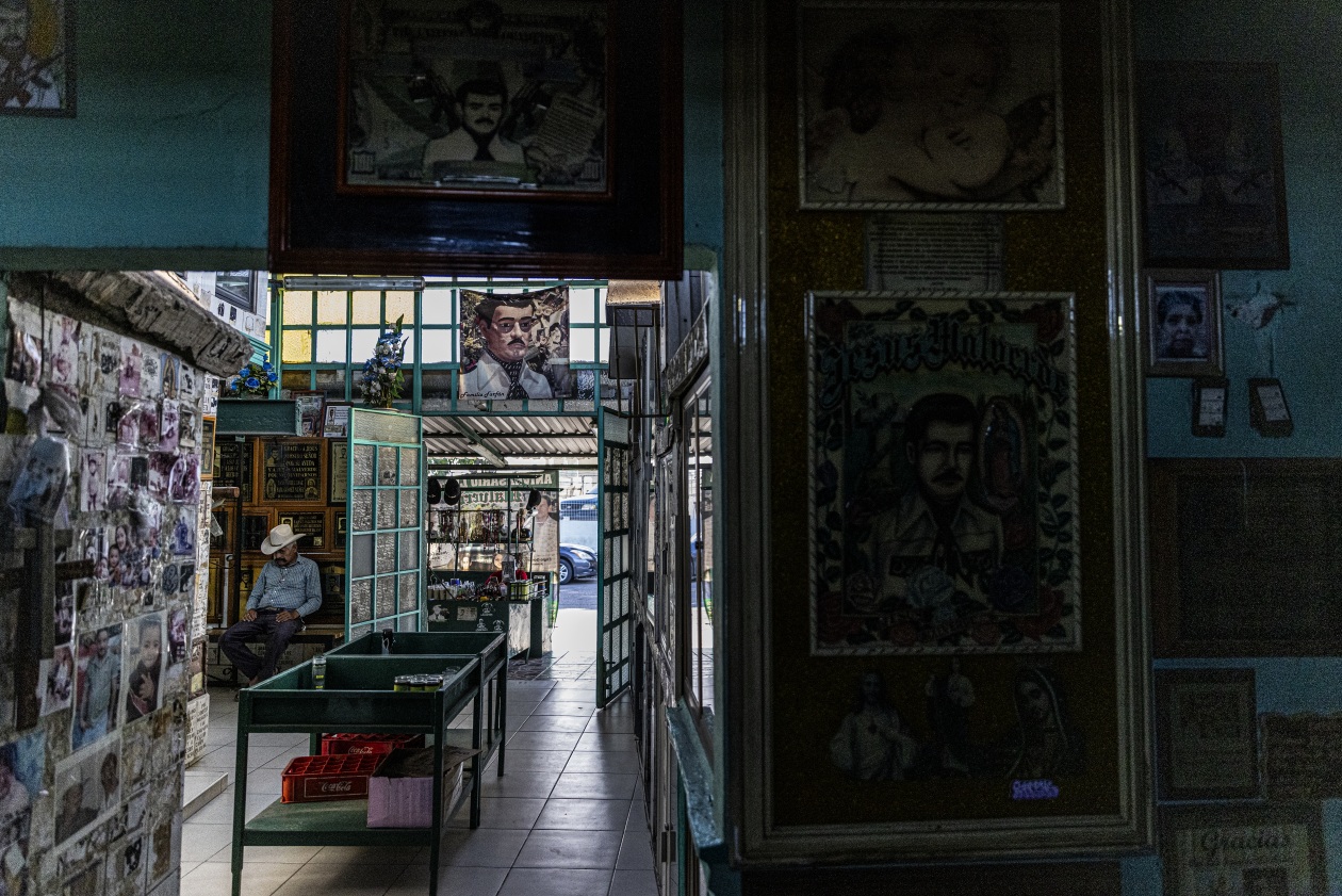 La capilla Malverde en Culiacán, decorada con retratos y fotografías, donde se encuentra sentado un hombre con sombrero de vaquero.