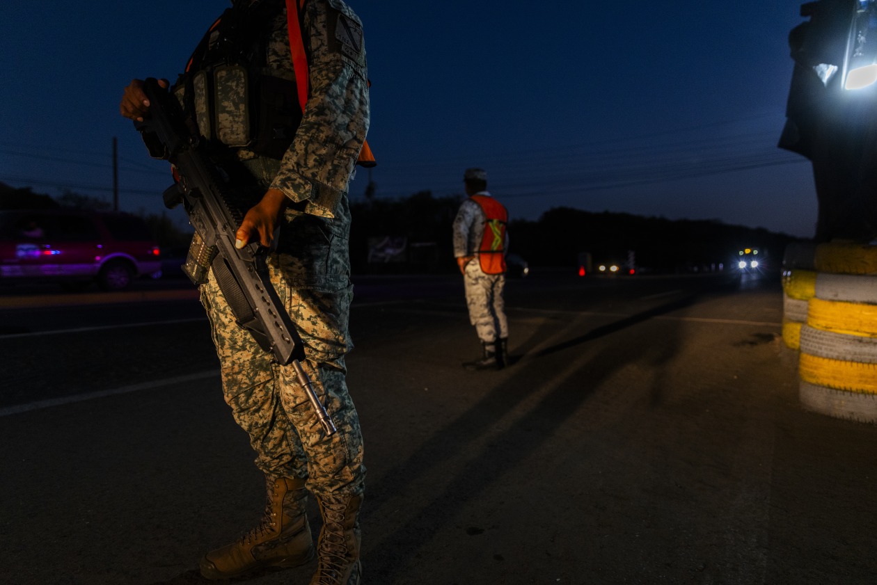 Soldado con uniforme de camuflaje y rifle en un puesto de control nocturno.