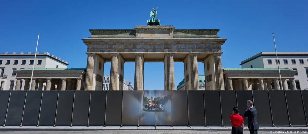 Dos personas contemplan el sitio conmemorativo de los 65 años del inicio de la construcción del Muro de Berlín, en la Puerta de Brandeburgo. (12.08.2026).